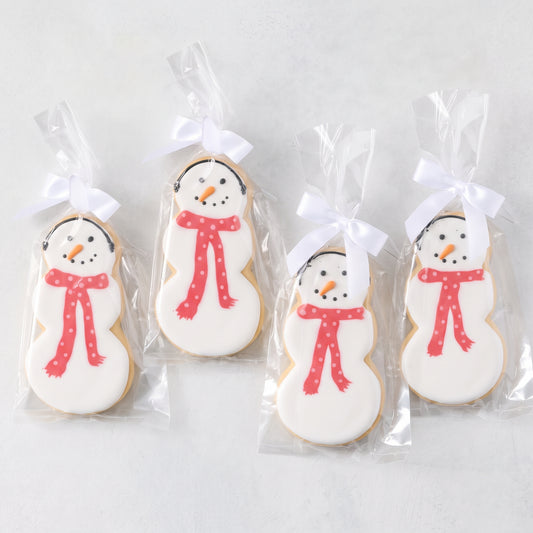 Set of four oversized snowman-shaped sugar cookies with white icing, orange carrot noses, and red polka-dot scarves in bags.