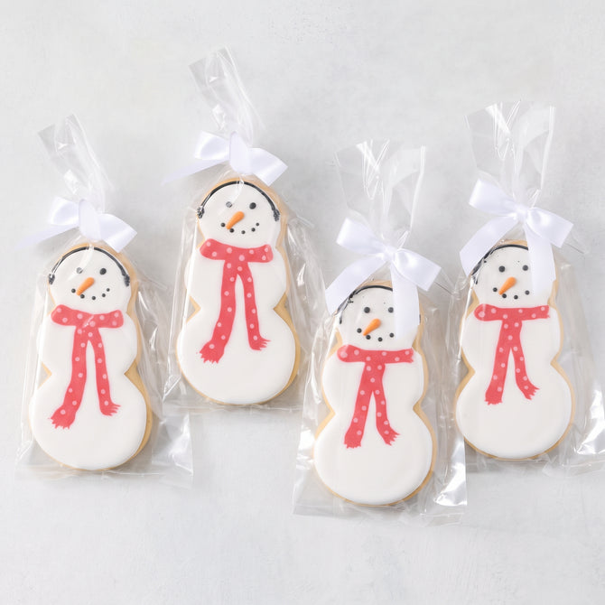 Set of four oversized snowman-shaped sugar cookies with white icing, orange carrot noses, and red polka-dot scarves in bags.