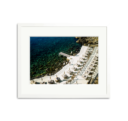 Il Pellicano Paradise framed wall art print of an Italian hotel's seaside terrace with lounge chairs and clear blue water.