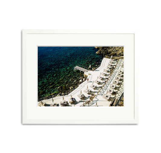 Il Pellicano Paradise framed wall art print of an Italian hotel's seaside terrace with lounge chairs and clear blue water.