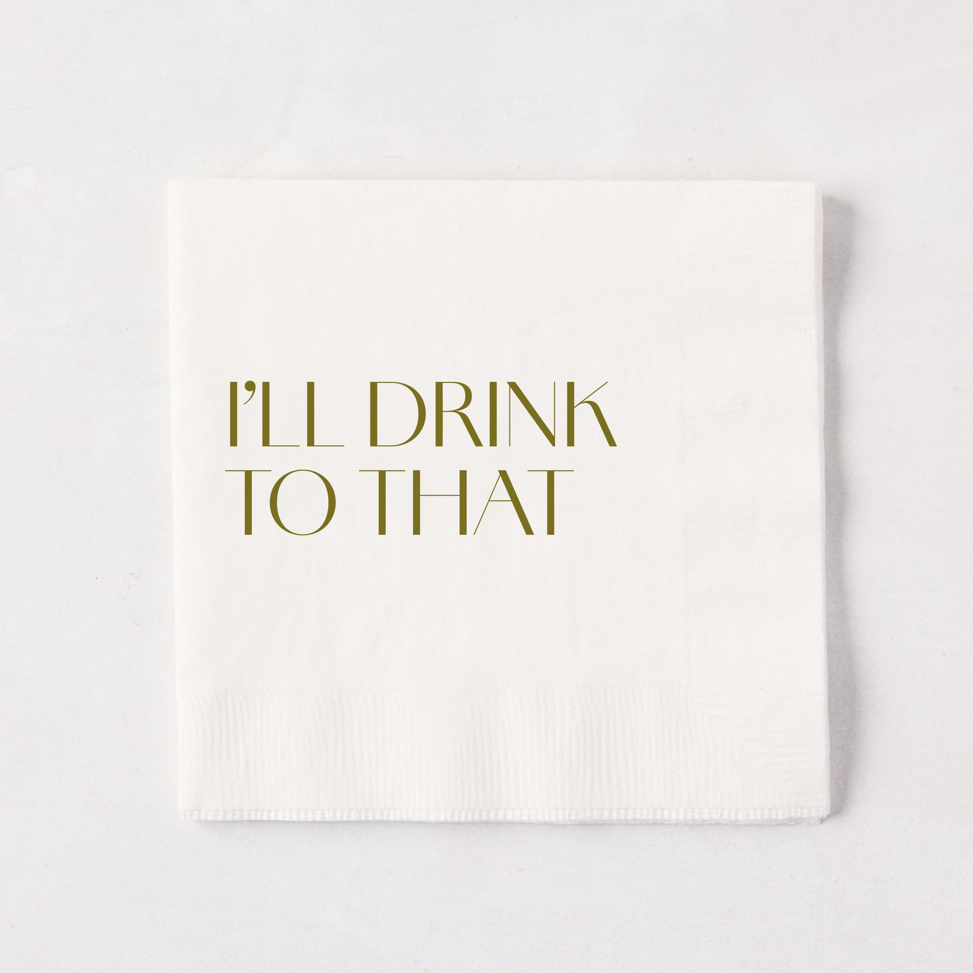 White 5.5" square paper cocktail napkin with "I'LL DRINK TO THAT" in gold text.