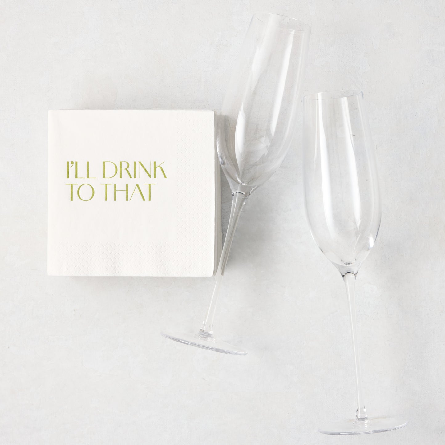 Two clear Heritage champagne glasses and white "I'll Drink To That" cocktail napkins on a light background.