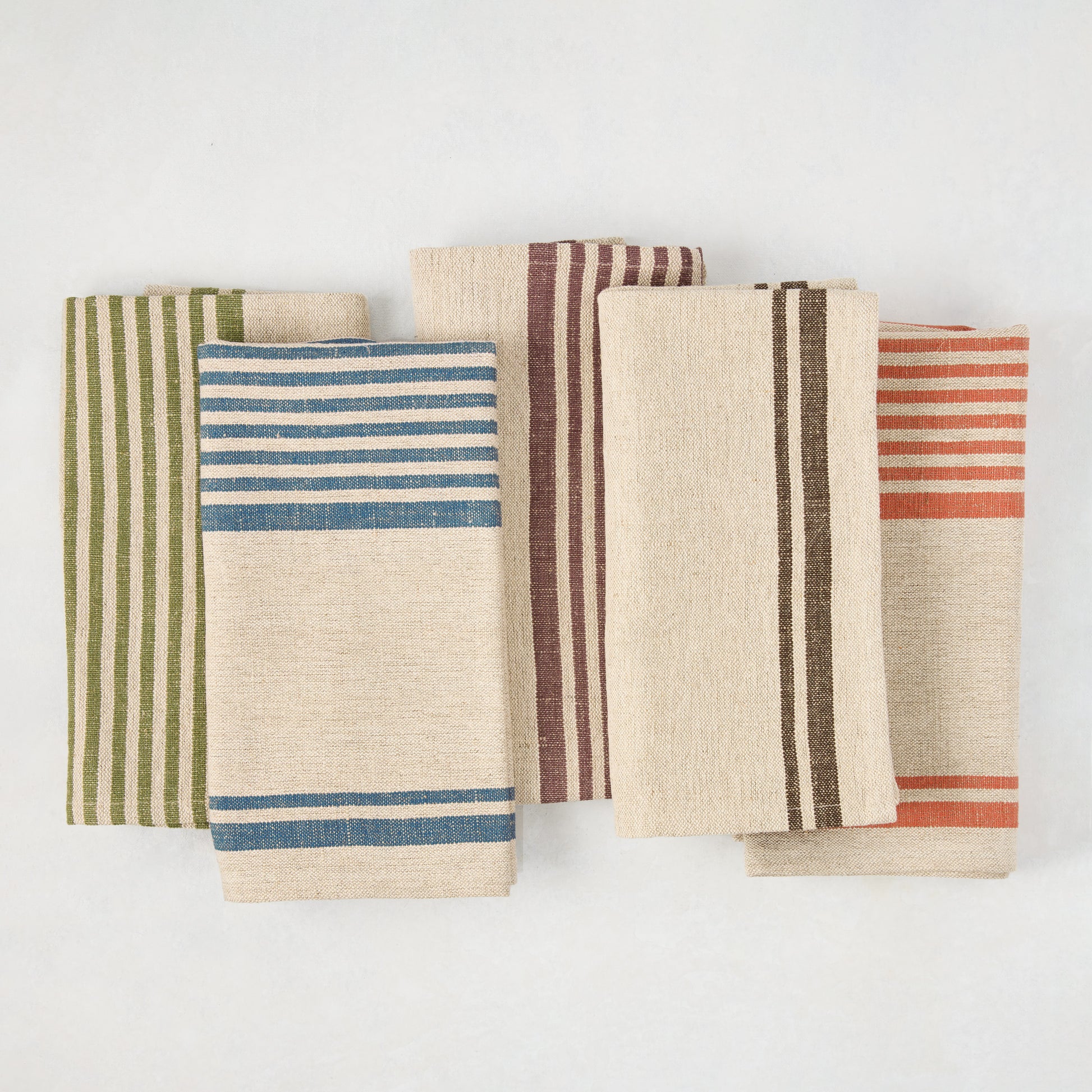 Five folded linen napkins with beige bases and vertical stripes in blue, green, plum, brown, and orange.