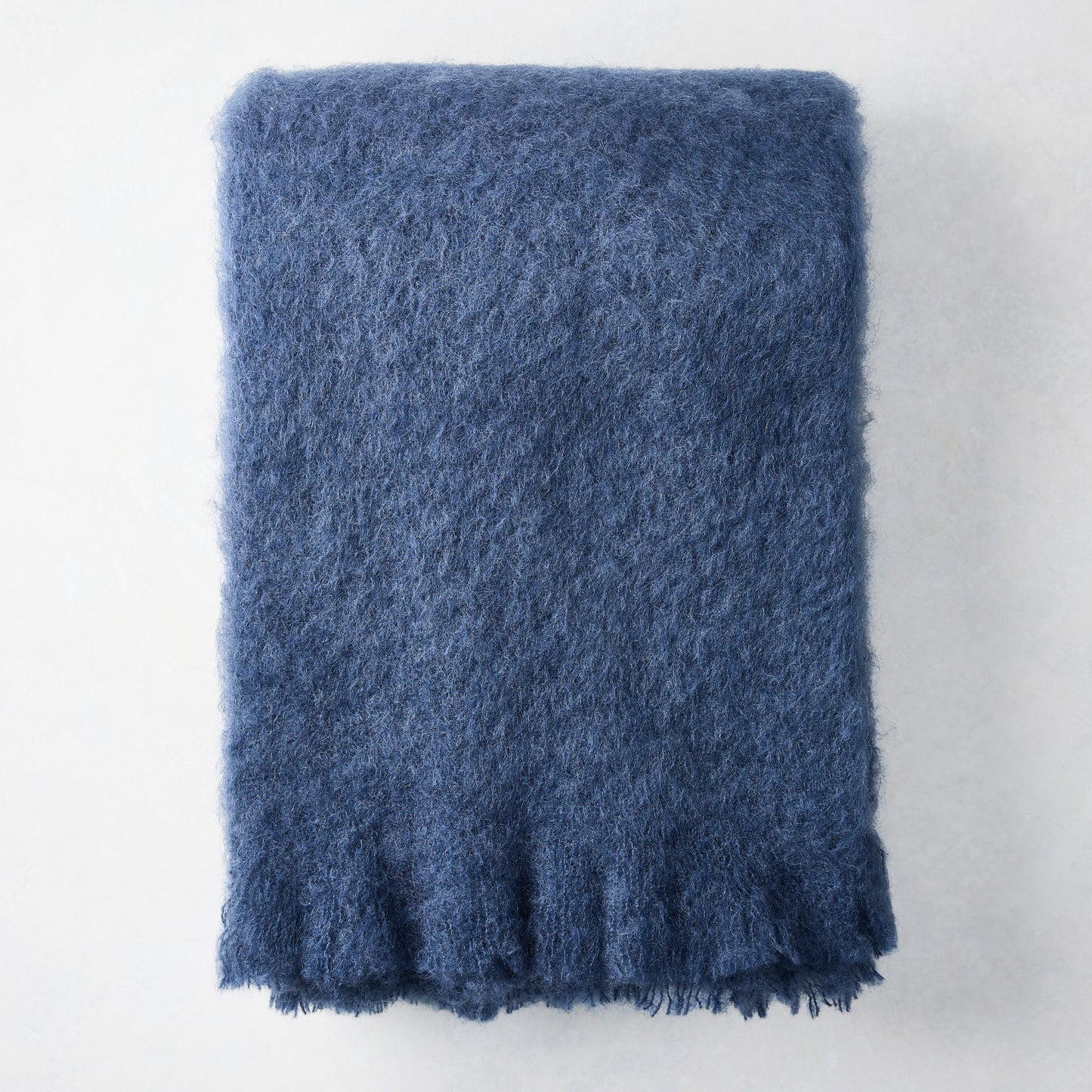 Folded indigo blue mohair throw blanket with a soft, shaggy texture.