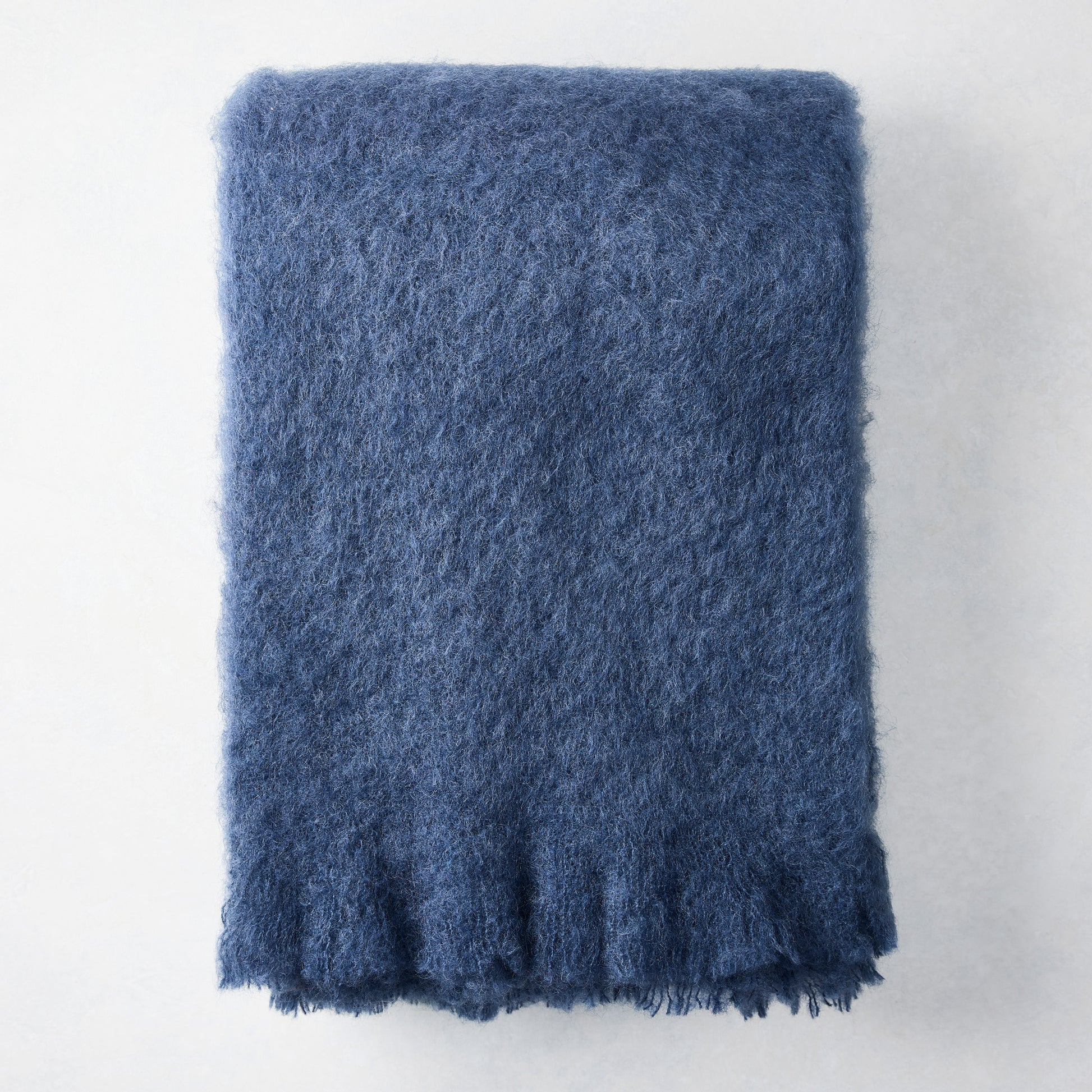 Folded indigo blue mohair throw blanket with a soft, shaggy texture.
