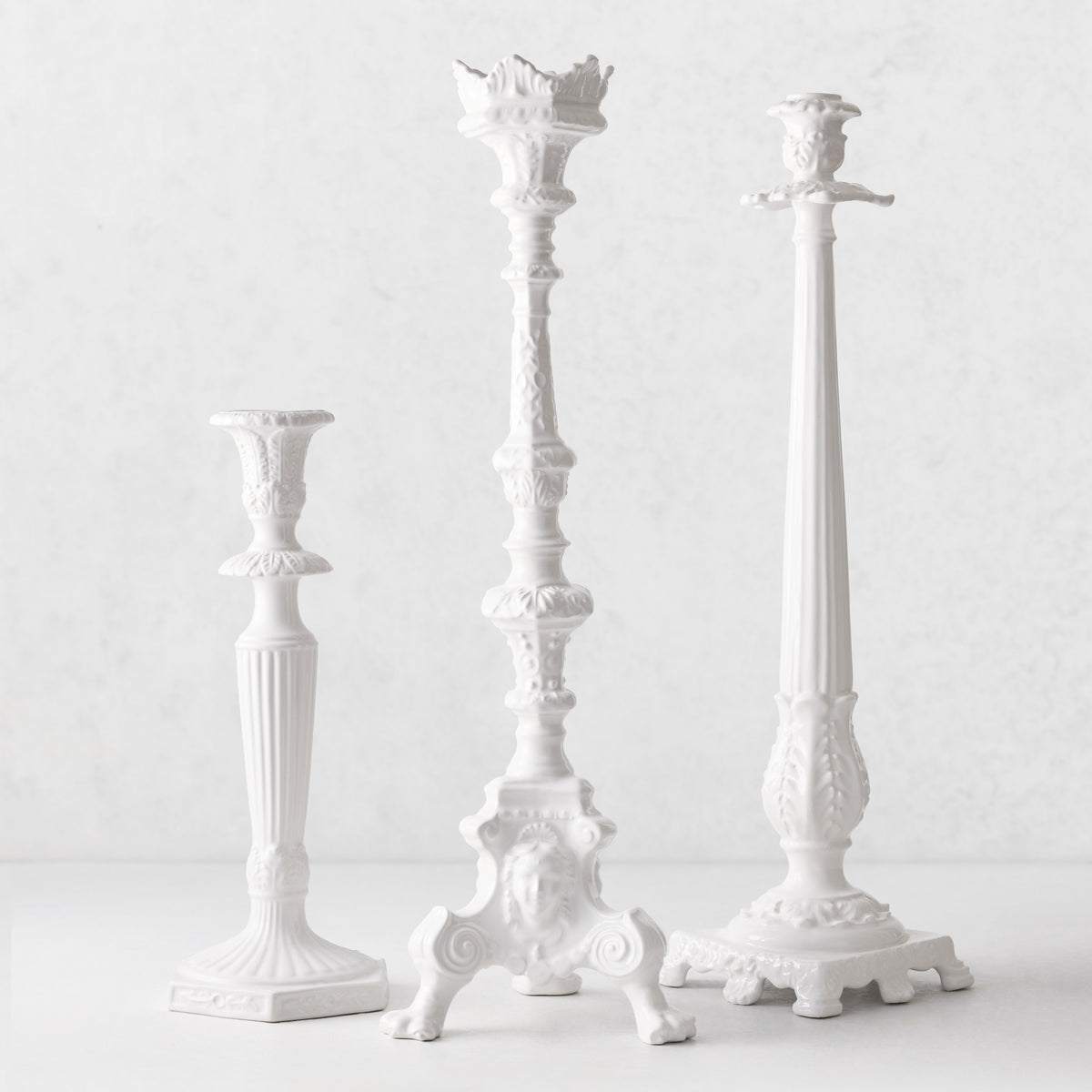 Three white Italian ceramic candlesticks with intricate antique-style detailing on a white background.