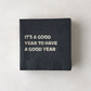 Black 5.5" square paper cocktail napkin with "It's a Good Year to Have a Good Year" in silver foil.