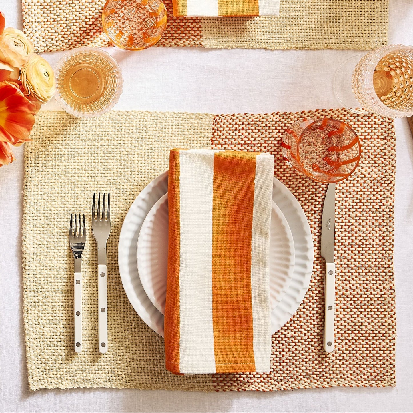Ivory bistro flatware set with stainless steel and acrylic handles arranged on a table setting with plates and napkins.