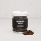 Jacobsen Salt Co. Tellicherry peppercorns in a clear glass jar with a white lid and black label on a light surface.