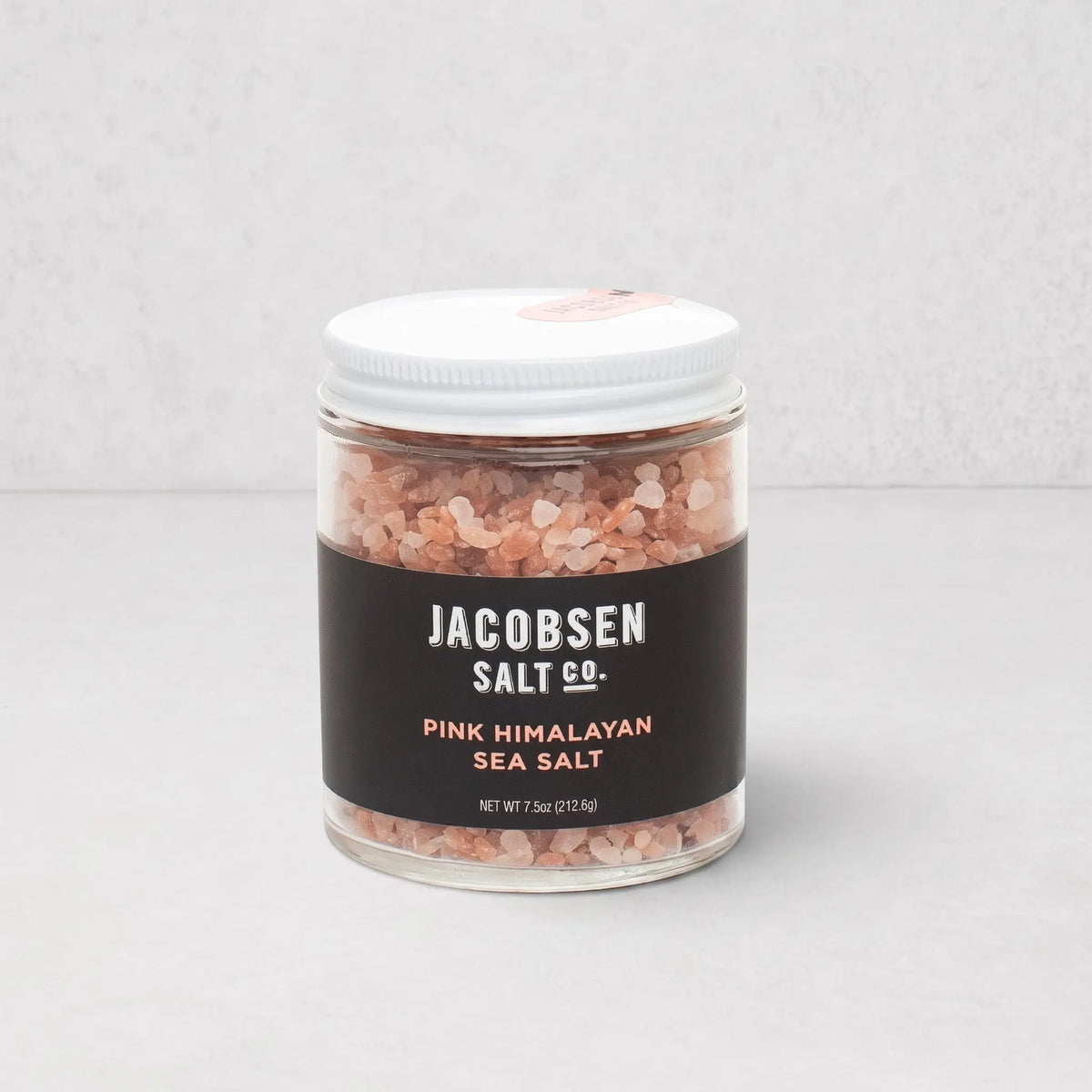 Jacobsen Salt Co. pink Himalayan salt crystals in a clear glass jar with a white lid and black label.
