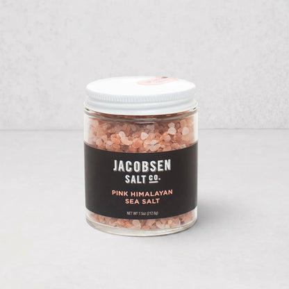 Jacobsen Salt Co. pink Himalayan salt crystals in a clear glass jar with a white lid and black label.
