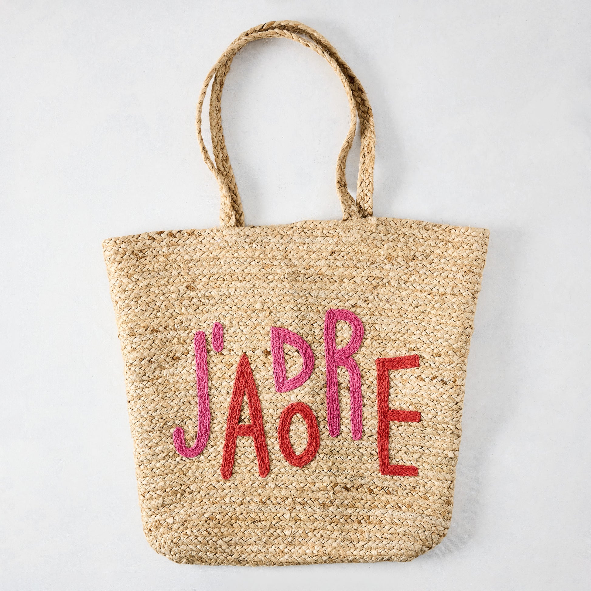 Natural jute woven tote bag with "J'ADORE" embroidered in red and pink.