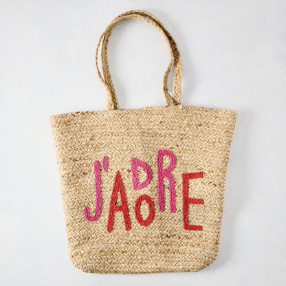 Natural jute woven tote bag with "J'ADORE" embroidered in red and pink.