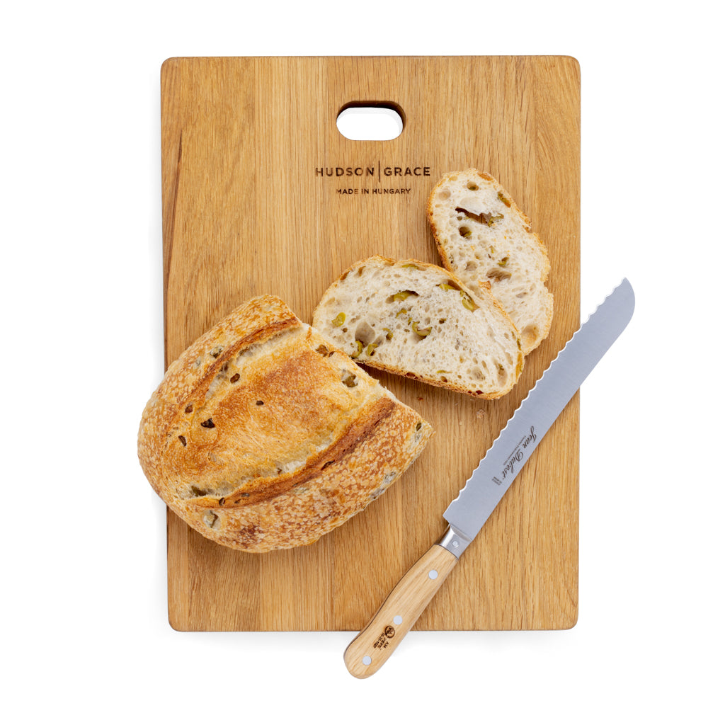 Jean Dubost bread knife with serrated stainless steel blade and light oak wood handle, next to sliced bread on a wood cutting board.