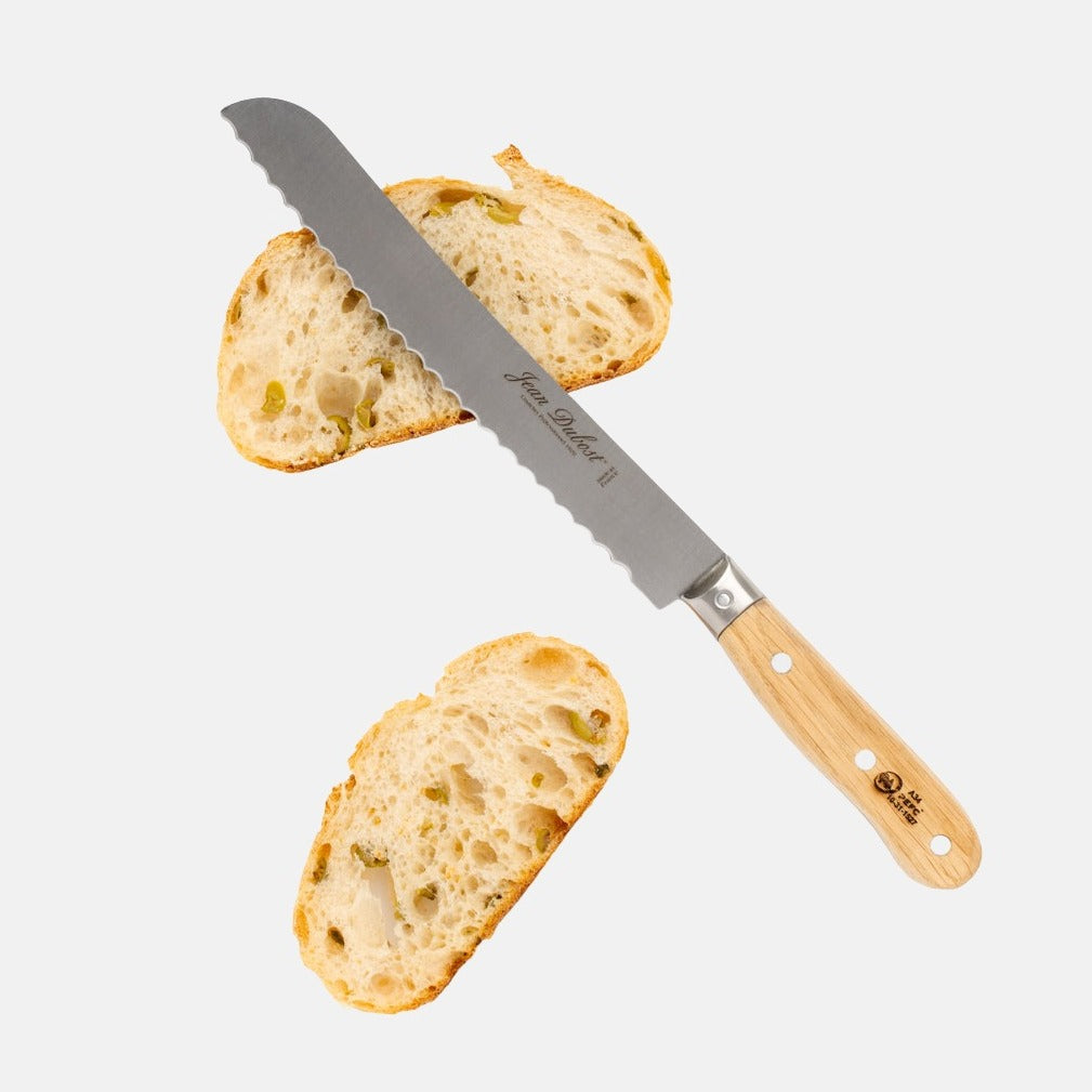Jean Dubost bread knife with serrated stainless steel blade and light oak wood handle, next to two slices of bread.