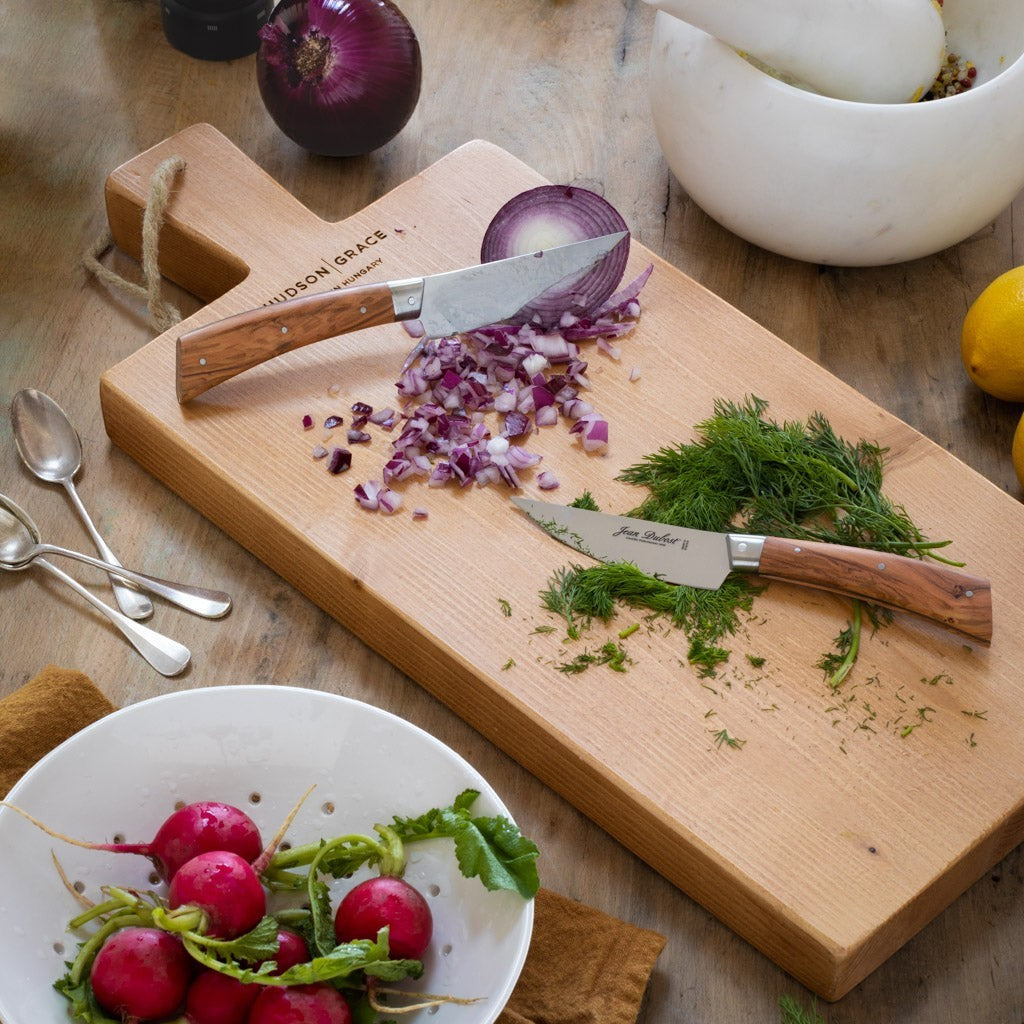 Jean Dubost Laguiole olive wood steak knives with stainless steel blades on a cutting board with chopped red onion and dill.