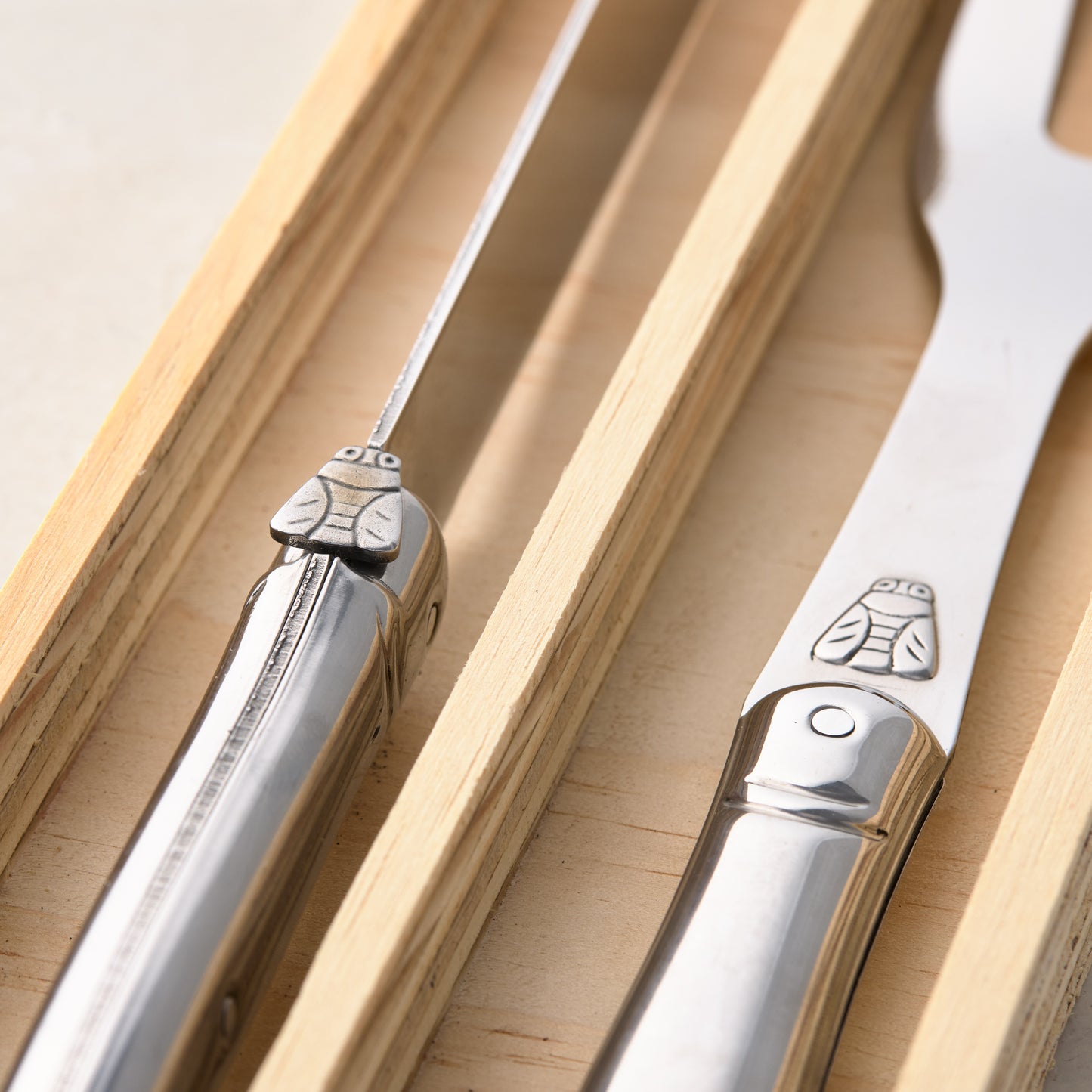 Jean Dubost Laguiole stainless steel carving knife and fork with bee design in a wooden box.