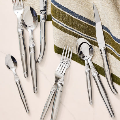 Jean Dubost Laguiole 5-piece stainless steel flatware set with iconic bee emblem on a striped napkin.
