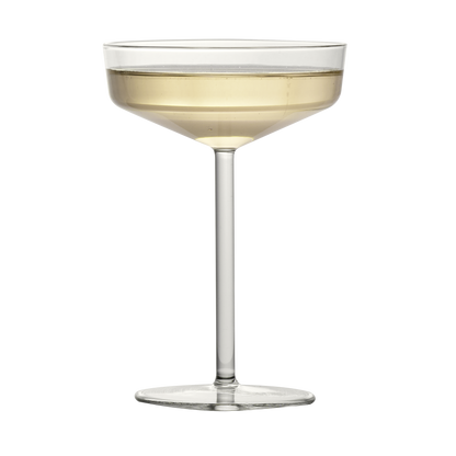 Modern clear glass coupe with a geometric bowl and thin stem, filled with a pale golden cocktail.