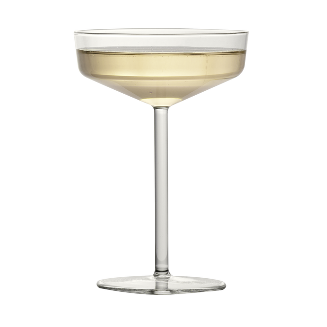 Modern clear glass coupe with a geometric bowl and thin stem, filled with a pale golden cocktail.