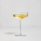 A clear coupe glass filled with a light golden drink and a lemon twist, centered on a clean light gray background.