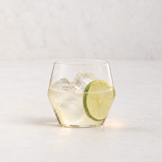 Clear glass Juniper double old fashioned glass with a geometric silhouette, filled with ice and a lime slice.