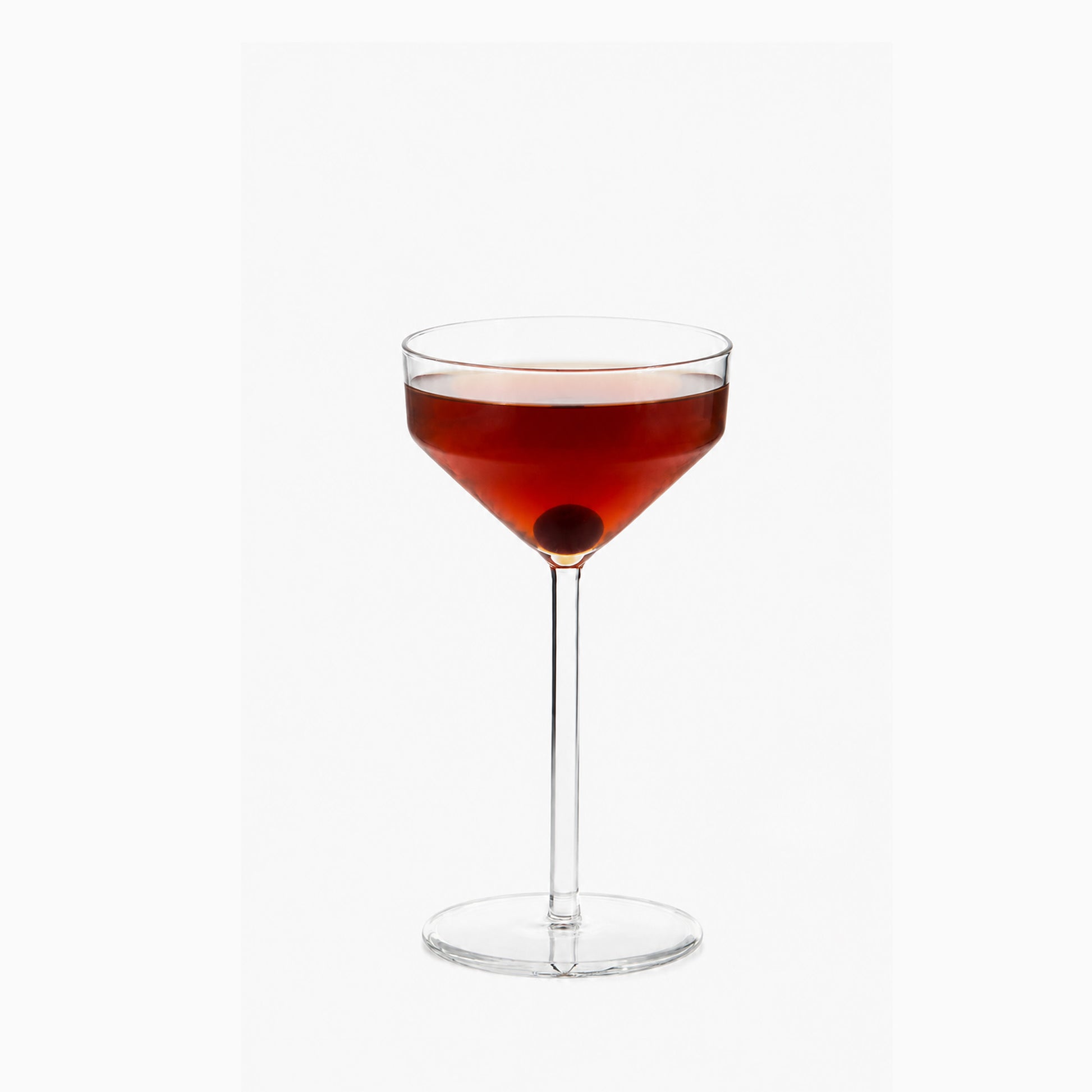 Juniper small cocktail glass with a geometric silhouette filled with a red drink and a cherry on a white background.