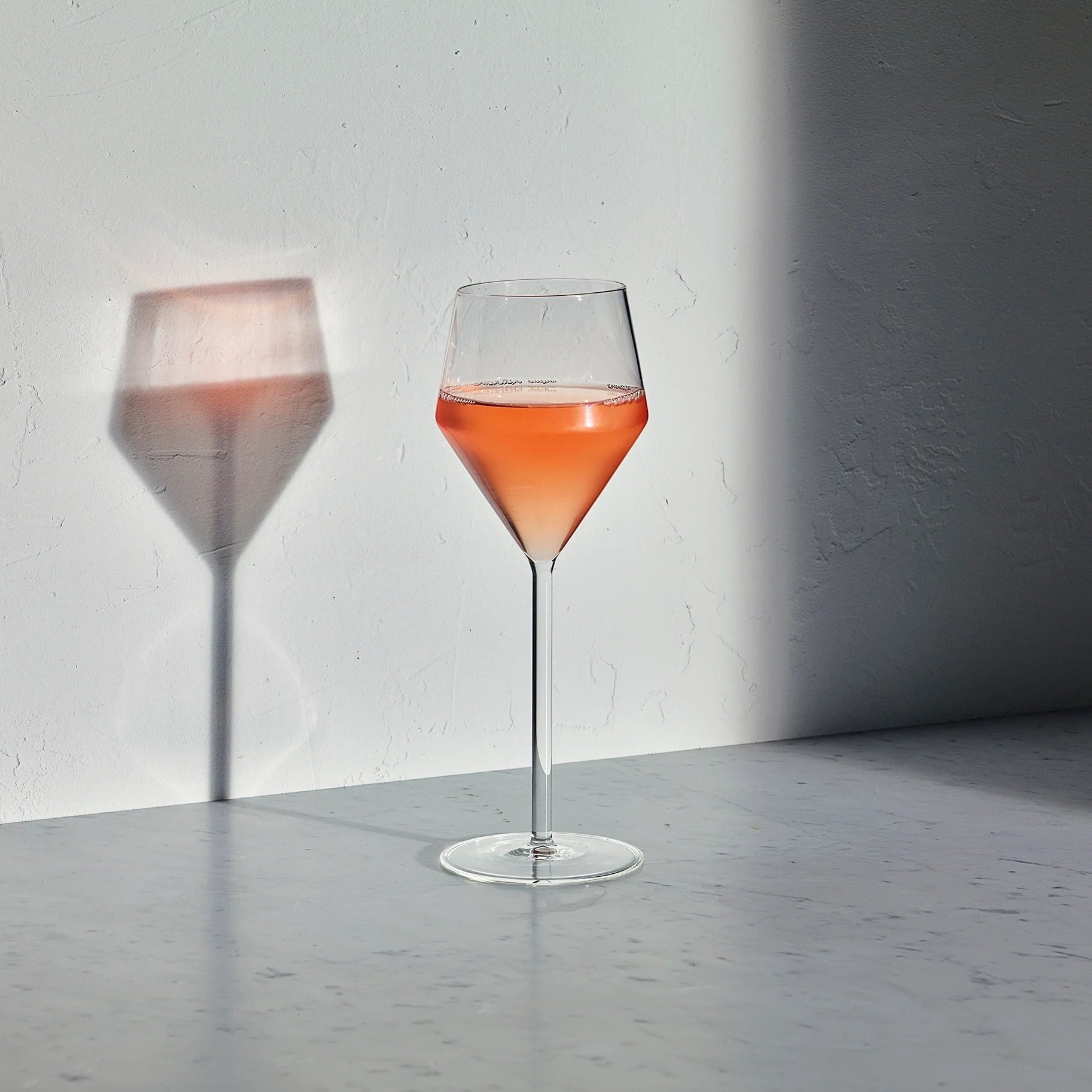 Hudson Grace Juniper white wine glass with a geometric silhouette and long stem filled with rose wine