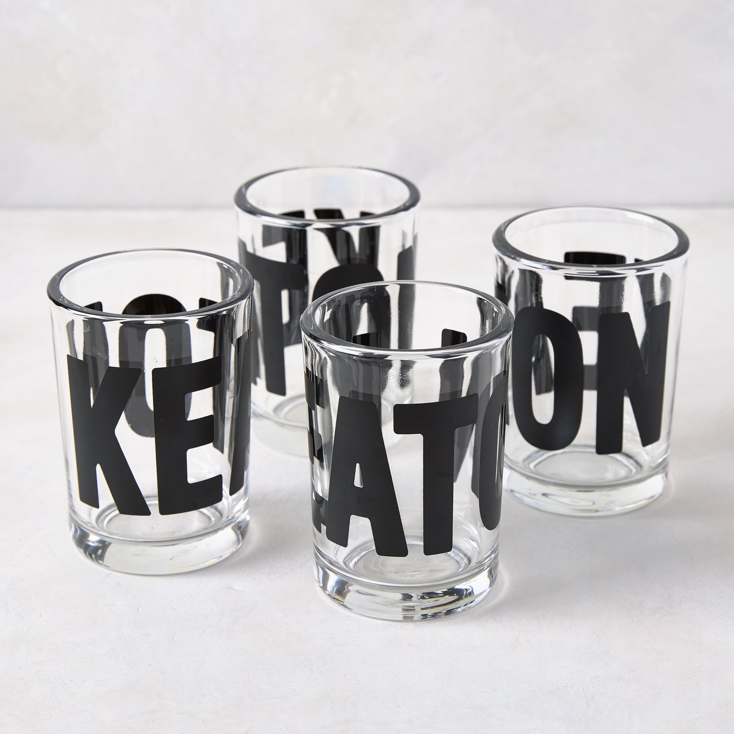 Four clear glass "Keaton" Everyday Wine Glasses with bold black lettering from Diane Keaton x Hudson Grace.
