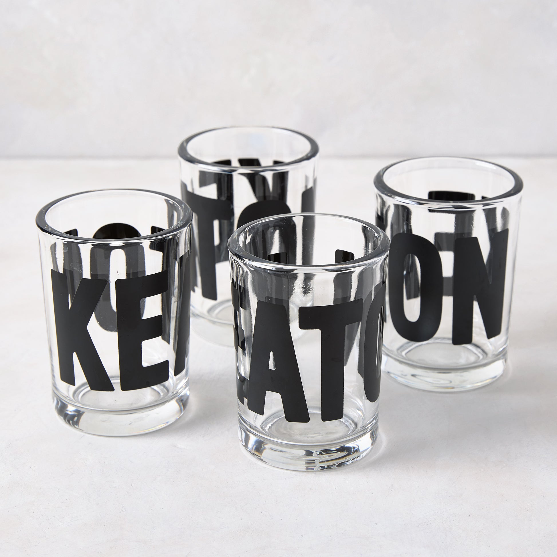 Four clear glass "Keaton" Everyday Wine Glasses with bold black lettering from Diane Keaton x Hudson Grace.