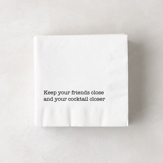 White 3-ply paper cocktail napkins with "Keep your friends close and your cocktail closer" in black text.