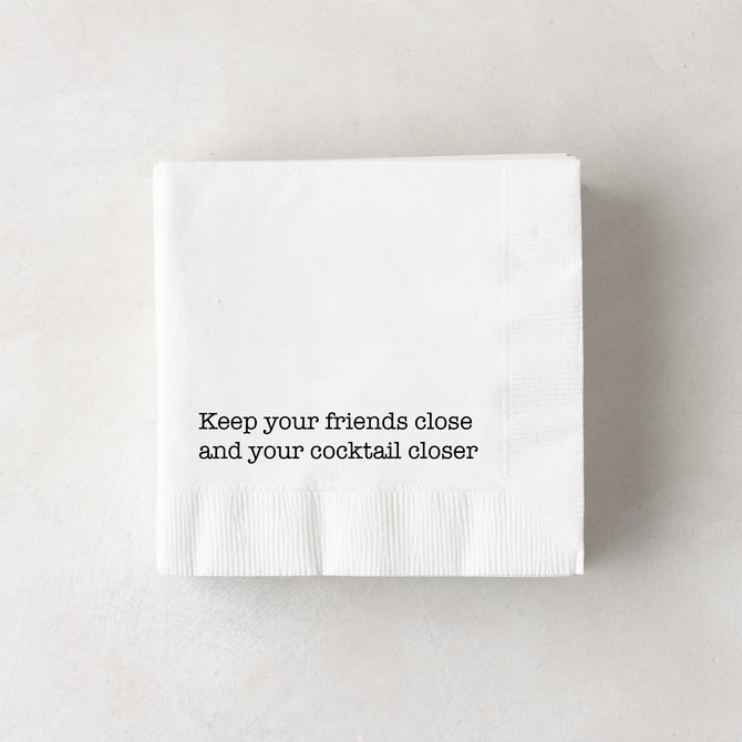 White 3-ply paper cocktail napkins with "Keep your friends close and your cocktail closer" in black text.