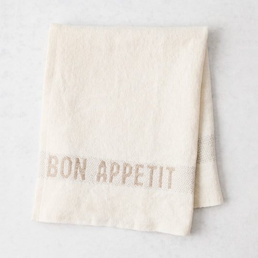 Folded off-white linen napkin with "BON APPETIT" in khaki lettering, 14"L x 18"W.