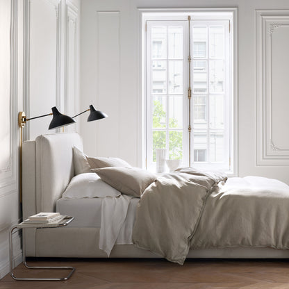 Khaki washed-linen pillow shams and duvet cover on a bed with white sheets in a bright bedroom.