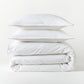 White percale duvet set with khaki piping, stacked neatly. Includes duvet cover and two shams.
