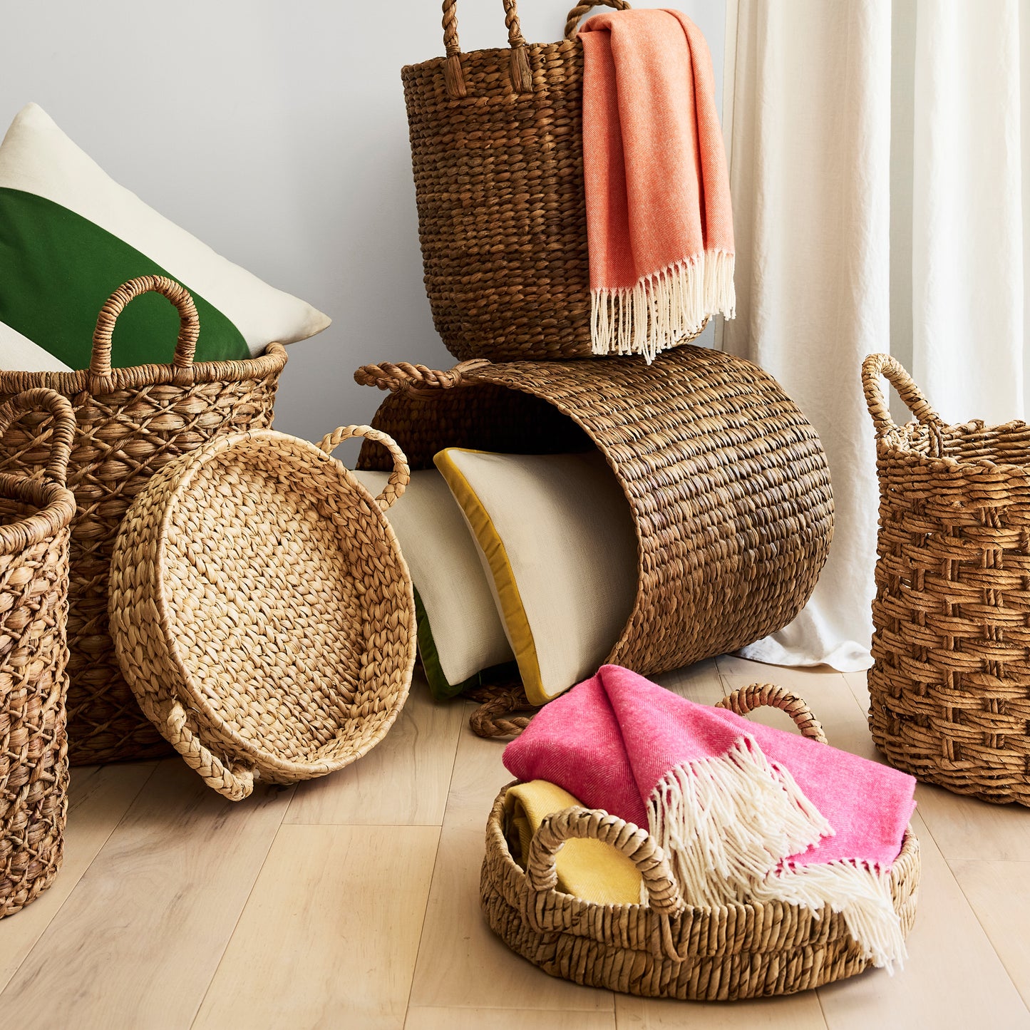 Woven baskets with handles holding cream and green pillows, and pink and orange fringed throws.