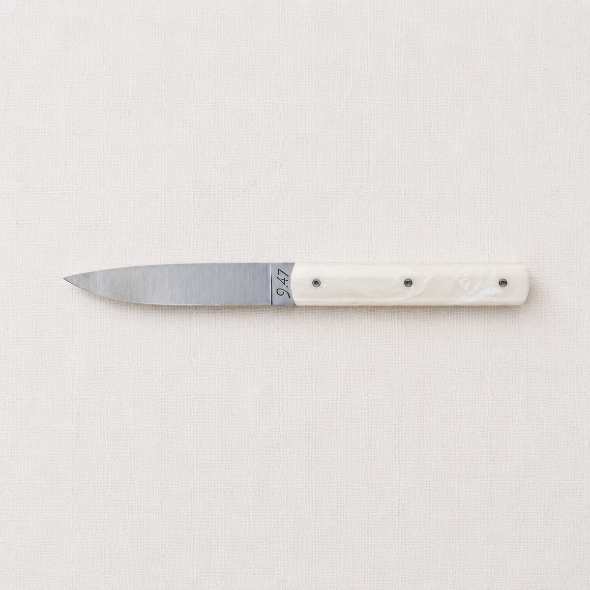 Perceval 9.47 stainless steel table knife with a sleek coffee creme Krion handle on a neutral fabric background.