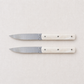 Set of two Perceval 9.47 steak knives with stainless steel blades and cream-colored Krion handles on a linen background.