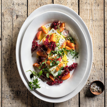 Oval white ceramic serving platter with raised edges, holding a fruit and cheese salad on a rustic wooden table.