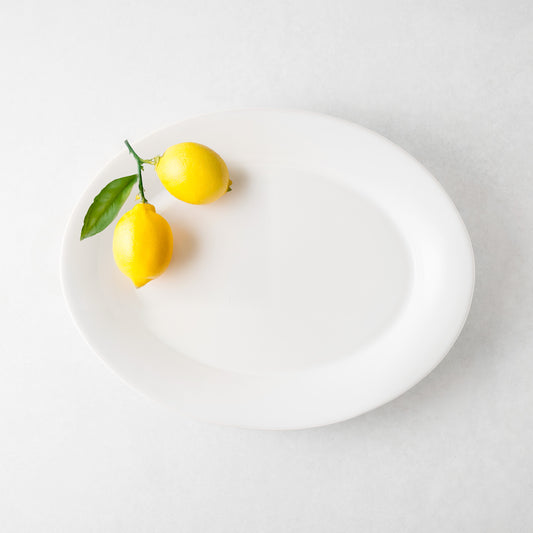 White oval ceramic serving platter with two bright yellow lemons and green leaves.