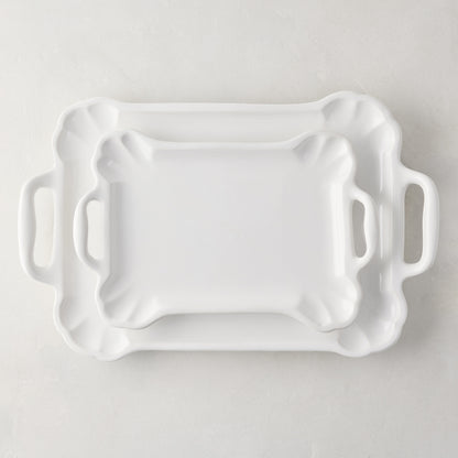 Large and small Alessia white ceramic serving platters with handles and detailed edges.