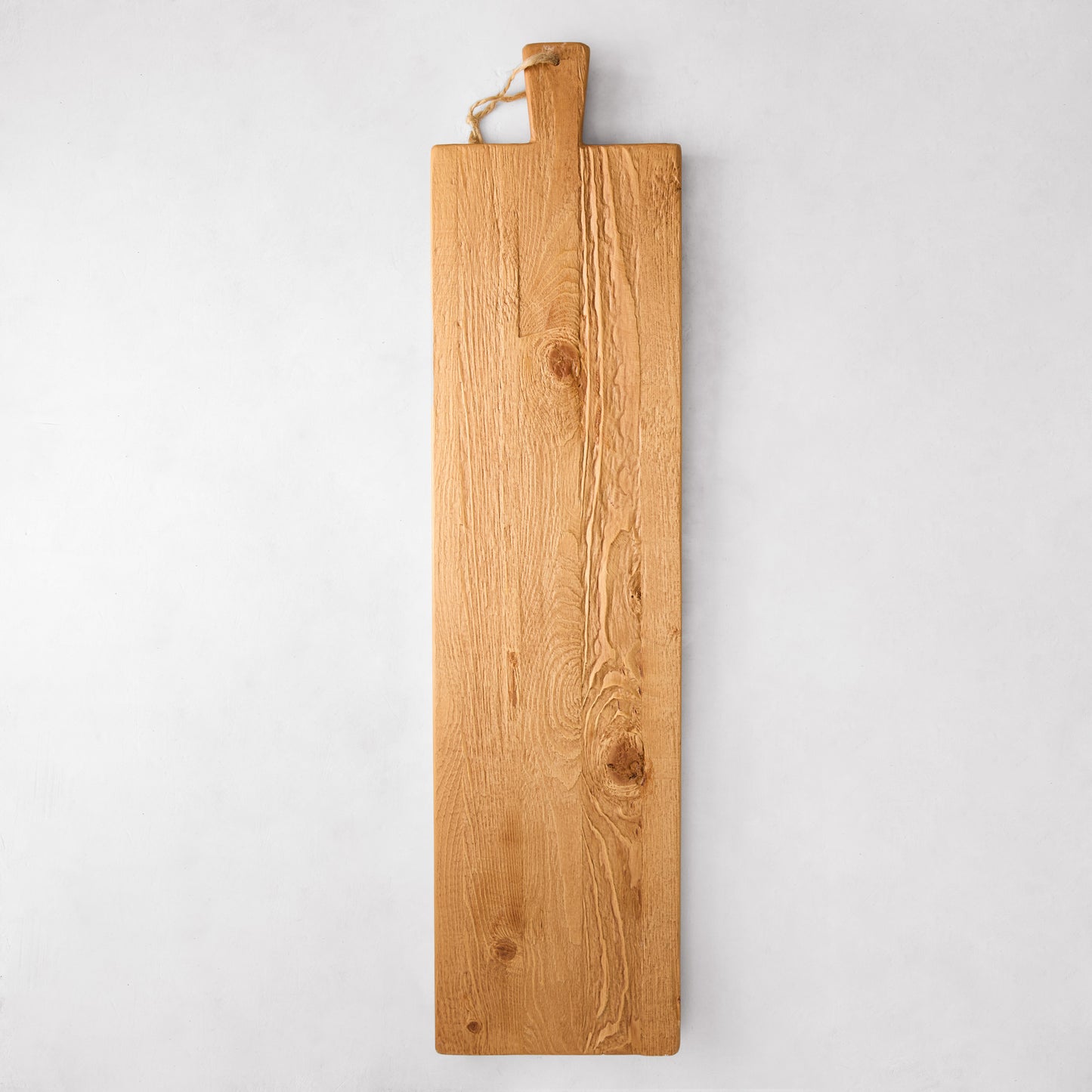 Long, rustic European pine wood serving plank with handle and rope, showing natural grain and knots.