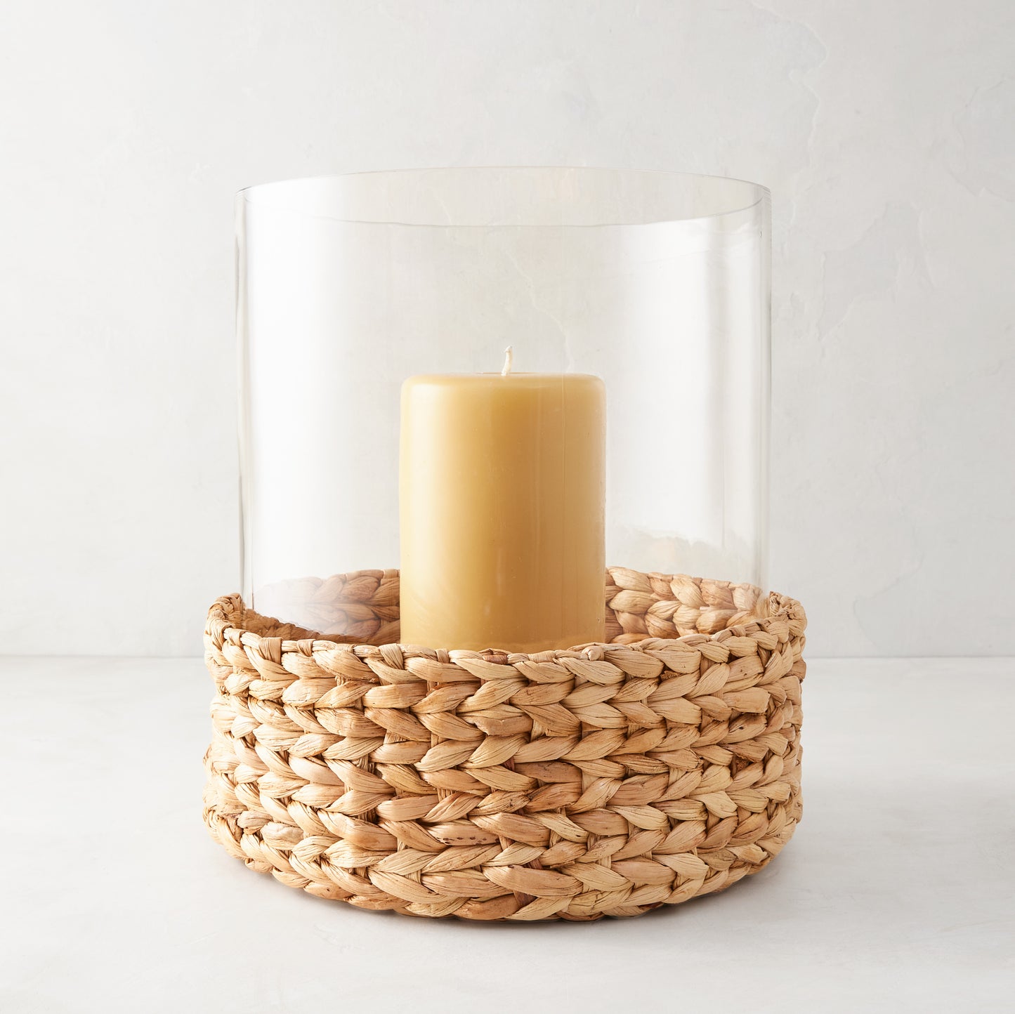 Large glass hurricane with woven water hyacinth base and amber candle.