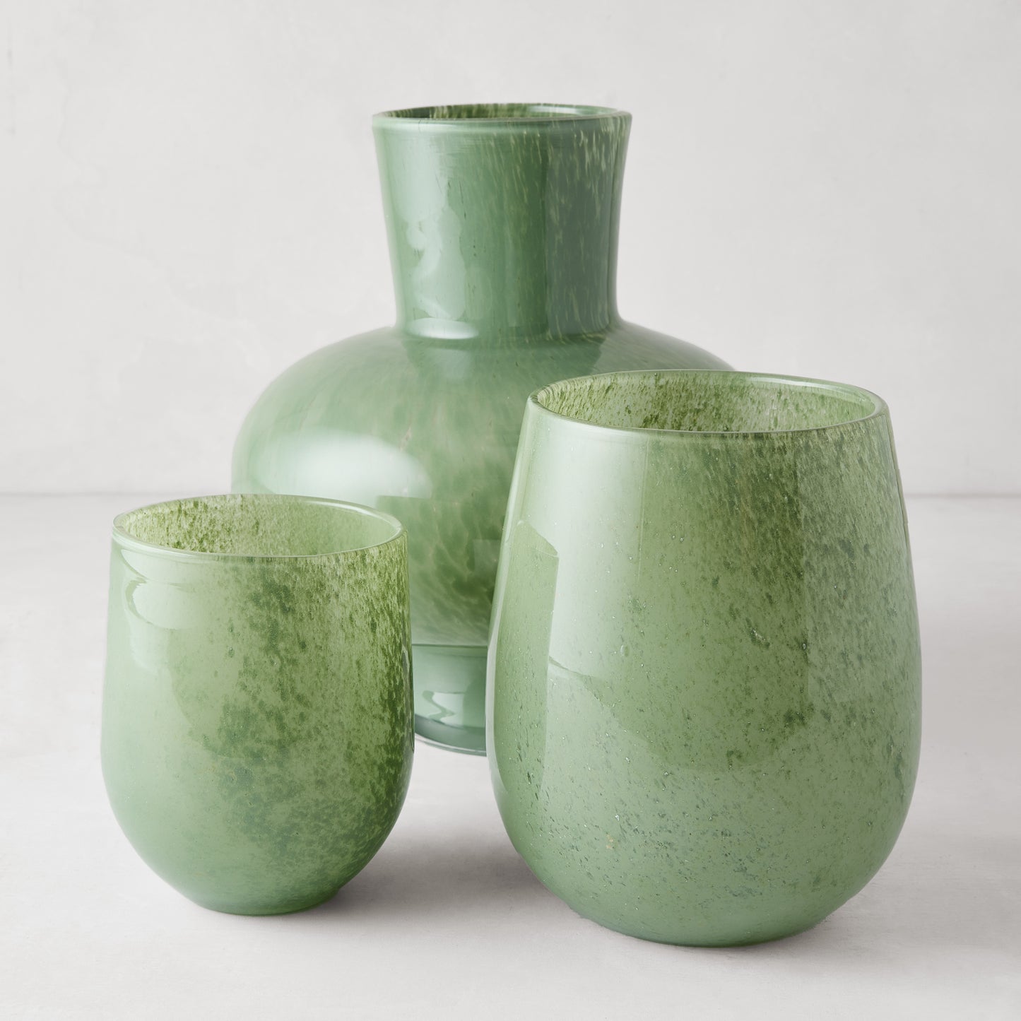 Three handblown opaque green glass barrel vases: one large, two smaller.