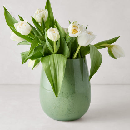 Large opaque green barrel glass vase with white tulips.