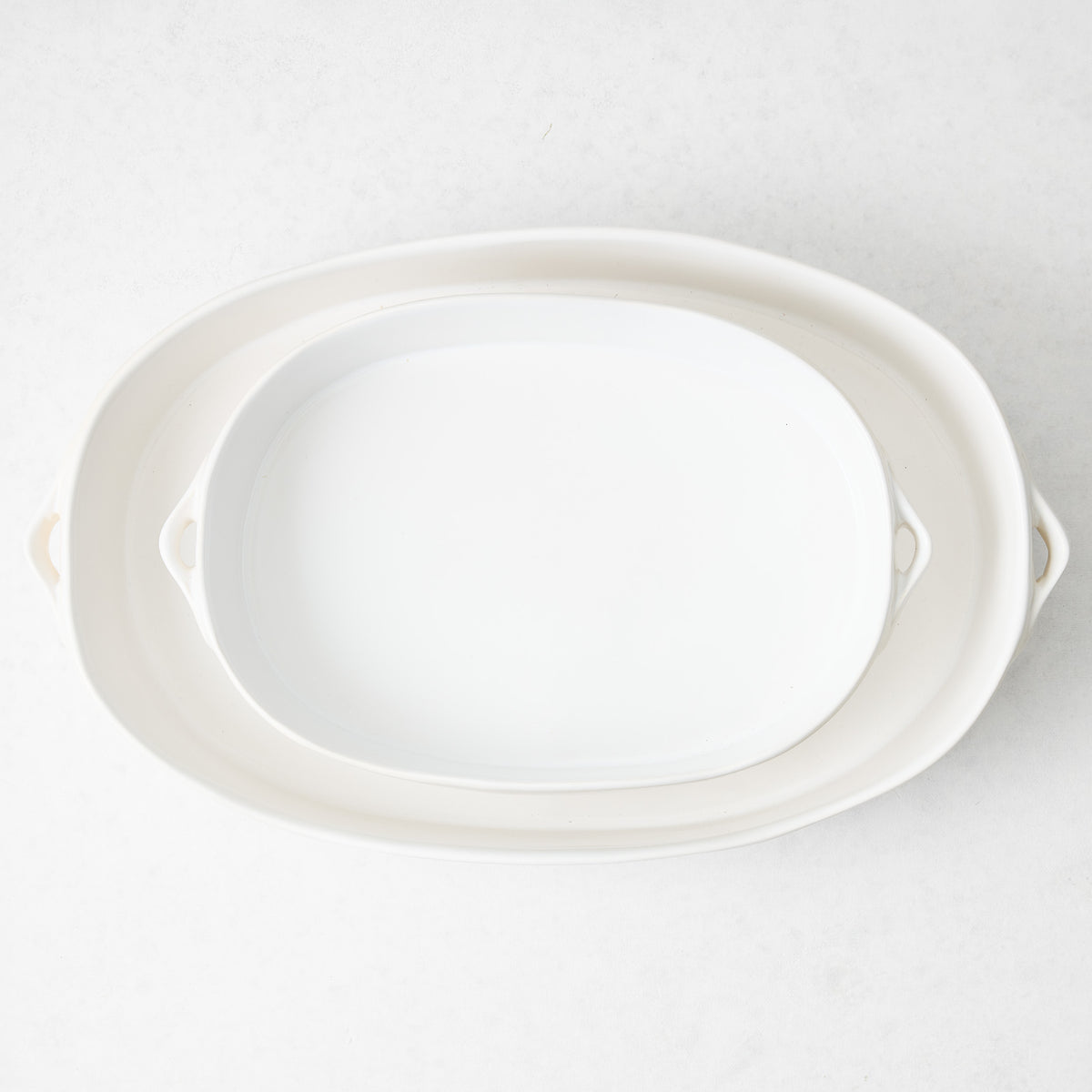 Large white oval stoneware baker with small side handles, viewed from above on a light background.