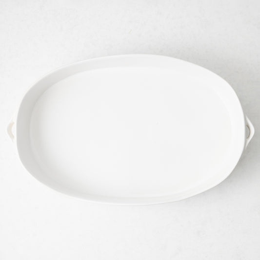 Large white oval stoneware baker with small side handles, top-down view on a neutral background.