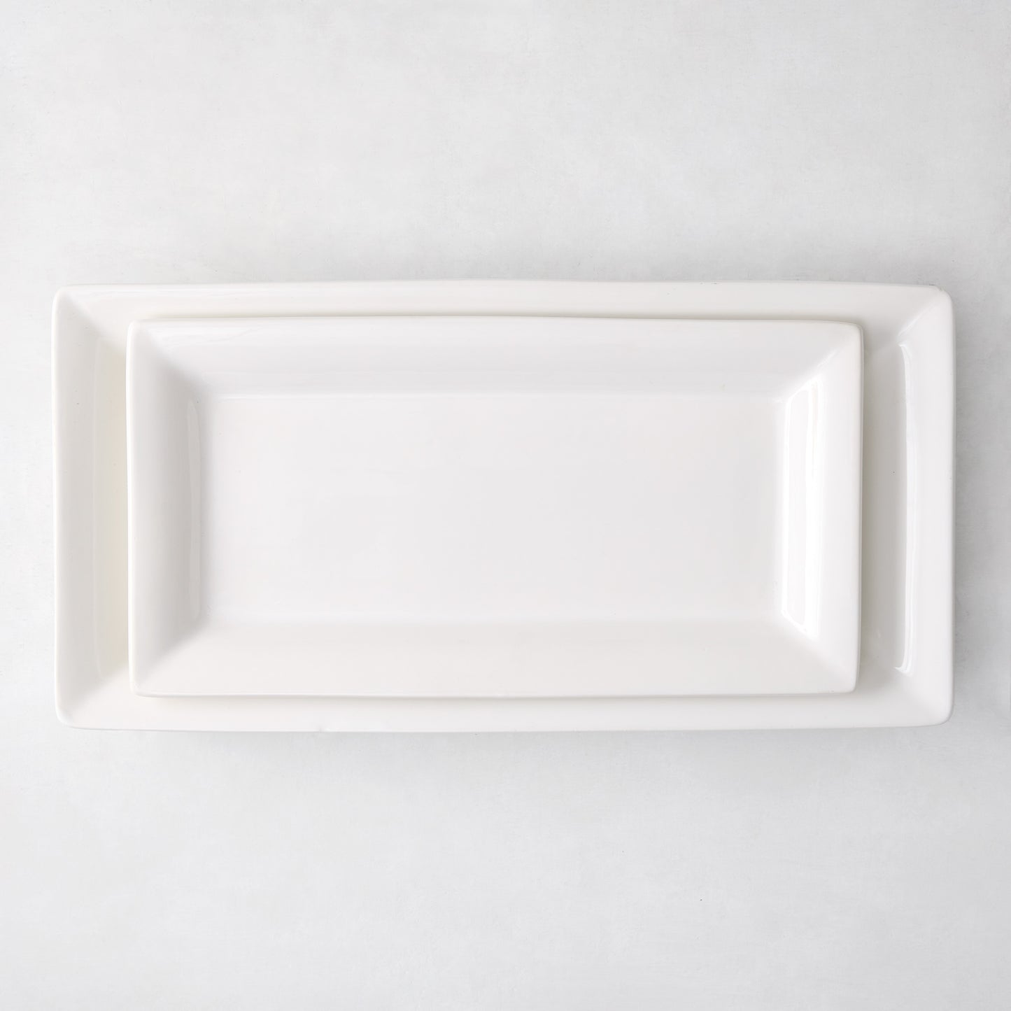 Two white ceramic Lucca rectangular serving platters, one nested inside the other, on a white background.