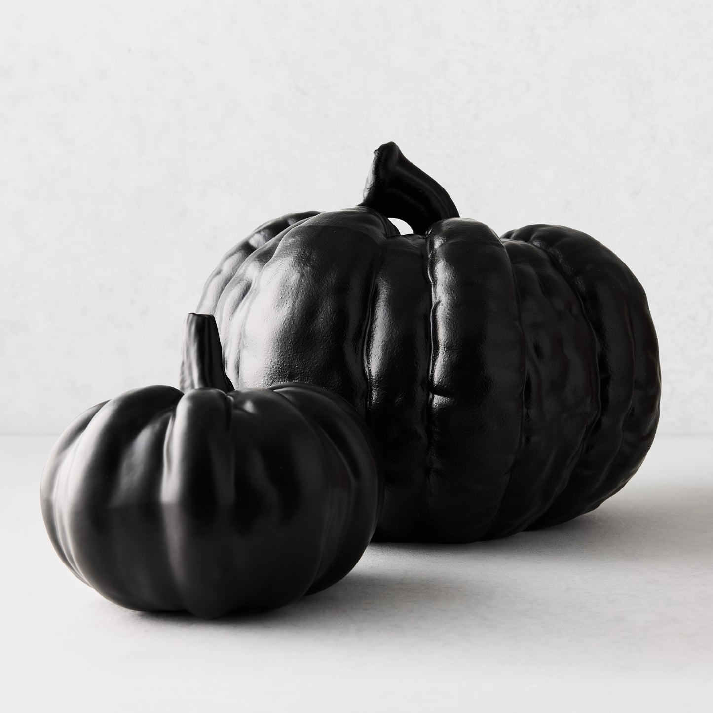 Two matte black ceramic pumpkins of different sizes with textured surfaces on a white background.