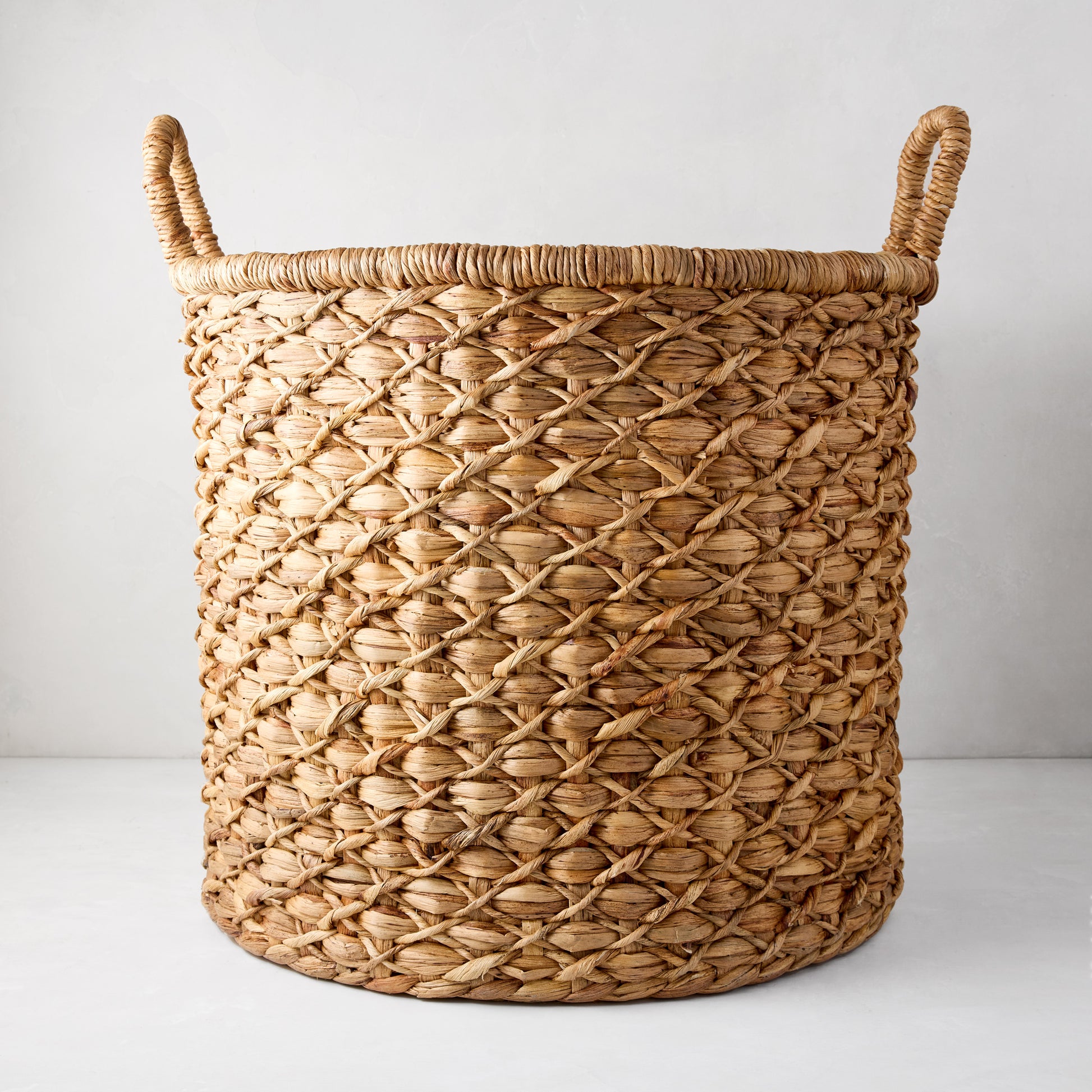 Large round handwoven hyacinth leaf basket with braided handles and diamond pattern.